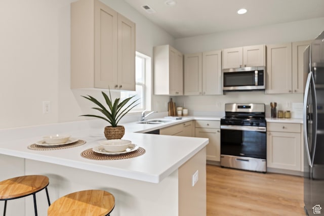 kitchen with a peninsula, light wood finished floors, recessed lighting, appliances with stainless steel finishes, and a sink