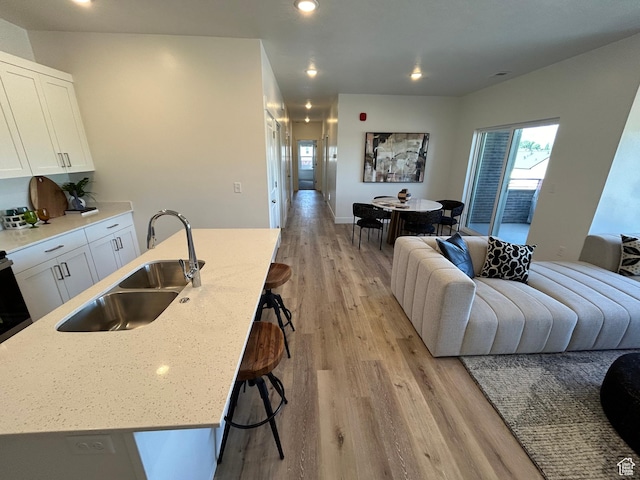 kitchen featuring white cabinetry, a kitchen island with sink, sink, and light hardwood / wood-style floors