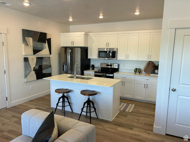 kitchen with appliances with stainless steel finishes, a breakfast bar, white cabinetry, an island with sink, and sink