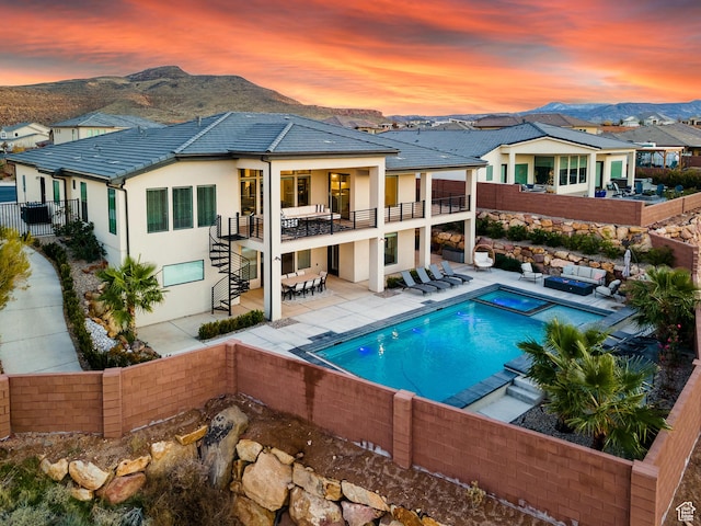 6026 S Zen Trail Way, St George, UT 84790 - back house at dusk with a balcony, a mountain view, a pool with hot tub, and a patio area