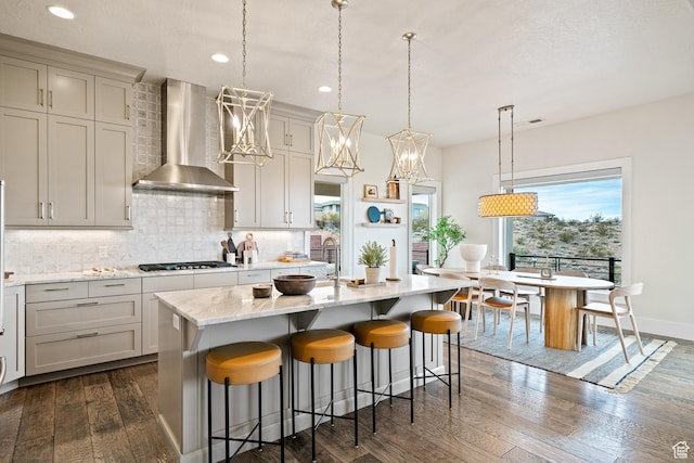 6026 S Zen Trail Way, St George, UT 84790 - kitchen featuring wall chimney range hood, a kitchen island with sink, backsplash, hanging light fixtures, and black gas cooktop
