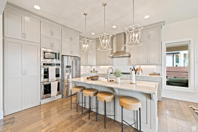 6026 S Zen Trail Way, St George, UT 84790 - kitchen featuring wall chimney exhaust hood, hanging light fixtures, a center island with sink, appliances with stainless steel finishes, and a kitchen breakfast bar