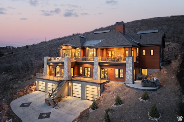 1310 Mellow Rd, Park City, UT 84060 - back of house featuring concrete driveway, a balcony, a chimney, an attached garage, and a shingled roof
