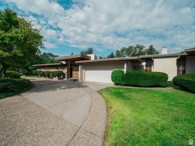 mid-century home featuring stucco siding, a chimney, a front lawn, and driveway