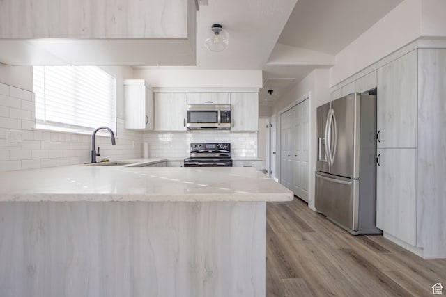 kitchen featuring sink, kitchen peninsula, stainless steel appliances, light hardwood / wood-style floors, and backsplash