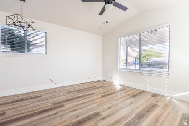 spare room with vaulted ceiling, ceiling fan with notable chandelier, and light wood-type flooring