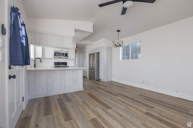 kitchen with light hardwood / wood-style flooring, appliances with stainless steel finishes, decorative backsplash, vaulted ceiling, and kitchen peninsula