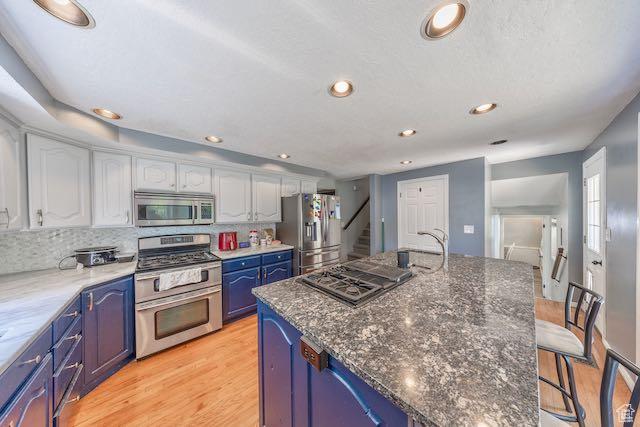 kitchen with white cabinets, decorative backsplash, light hardwood / wood-style floors, stainless steel appliances, and blue cabinetry