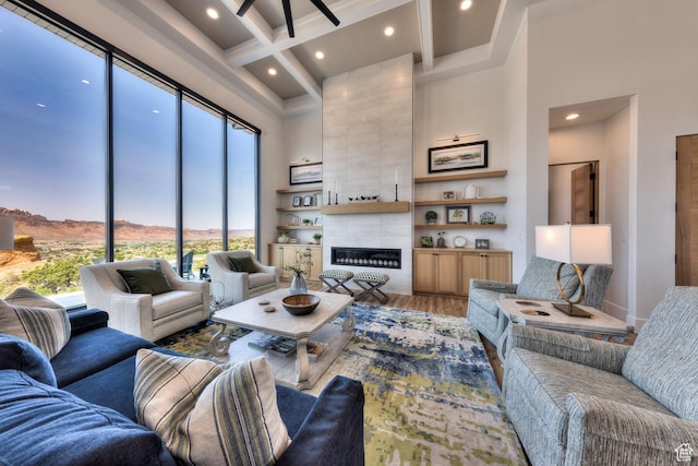 living room with coffered ceiling, a tiled fireplace, wood finished floors, a high ceiling, and beam ceiling