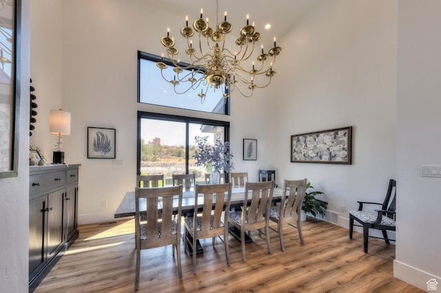 dining space featuring baseboards, light wood finished floors, a high ceiling, and a notable chandelier