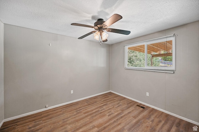 spare room with wood finished floors, a textured ceiling, baseboards, visible vents, and ceiling fan