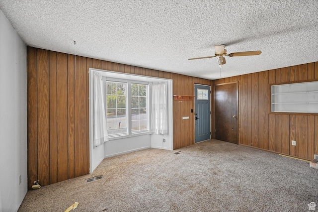 unfurnished room with carpet flooring, a ceiling fan, wood walls, a textured ceiling, and visible vents