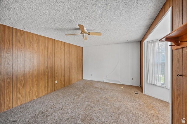 unfurnished room with wooden walls, ceiling fan, carpet, and a textured ceiling
