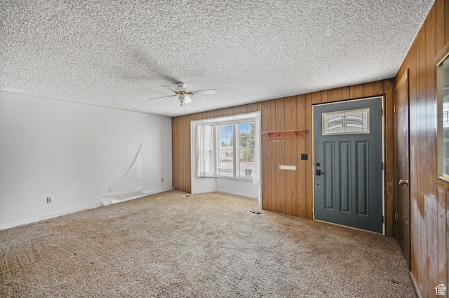 carpeted foyer with a textured ceiling, ceiling fan, visible vents, and wooden walls