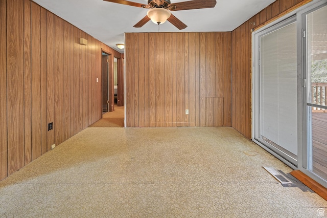 carpeted empty room featuring ceiling fan, visible vents, and wooden walls
