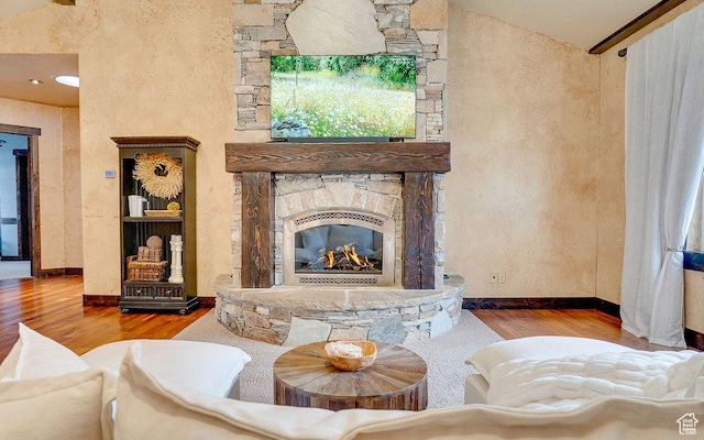 living area featuring vaulted ceiling, a stone fireplace, wood finished floors, and baseboards