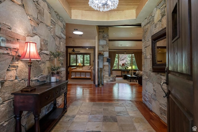 hall featuring a chandelier, stone finish floor, and a raised ceiling