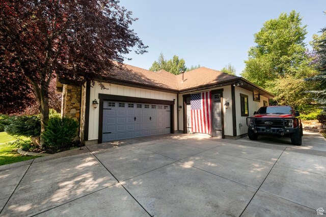 ranch-style house with a garage, stone siding, driveway, and a shingled roof