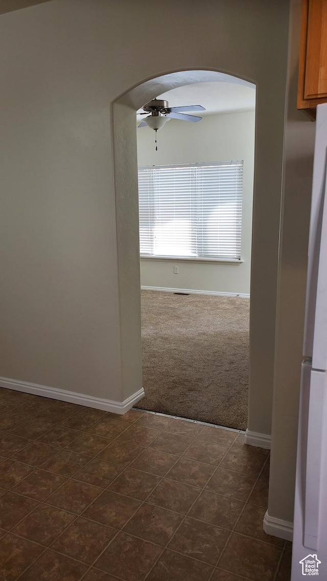 hall featuring arched walkways, dark colored carpet, and baseboards