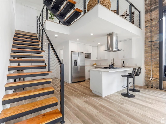 231 S Edison St E Unit 7, Salt Lake City, UT 84111 - kitchen featuring appliances with stainless steel finishes, wall chimney exhaust hood, a towering ceiling, white cabinets, and light wood-style flooring