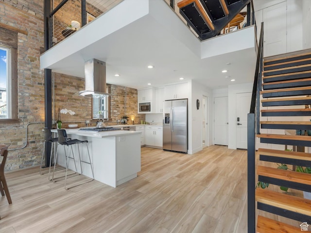 231 S Edison St E Unit 3, Salt Lake City, UT 84111 - kitchen featuring appliances with stainless steel finishes, island range hood, a peninsula, brick wall, and healthy amount of natural light