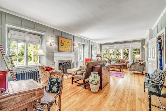 living room with radiator, crown molding, a fireplace, and light wood-type flooring