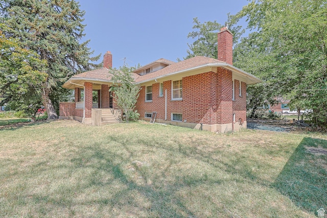 rear view of property with brick siding, a lawn, a porch, and a chimney