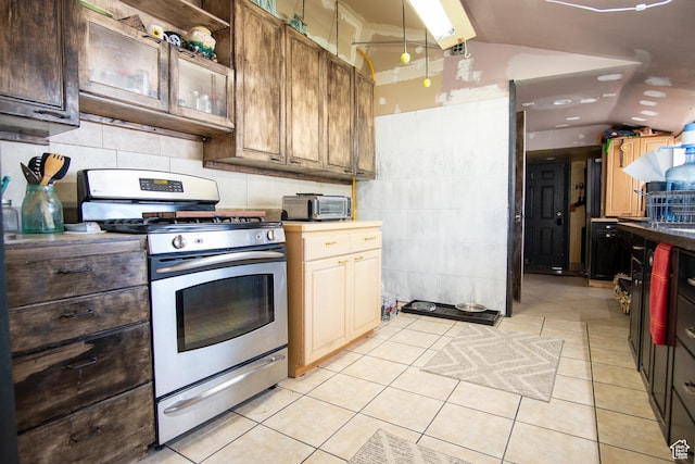 kitchen with vaulted ceiling, light tile patterned floors, stainless steel gas range, and decorative backsplash