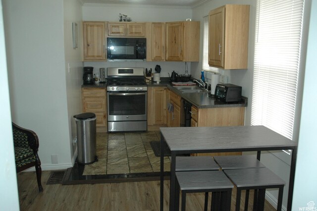kitchen featuring stainless steel gas stove, black microwave, light brown cabinetry, dark countertops, and a sink