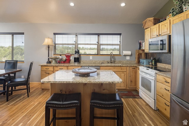 kitchen with light brown cabinets, a breakfast bar, a sink, stainless steel appliances, and a center island