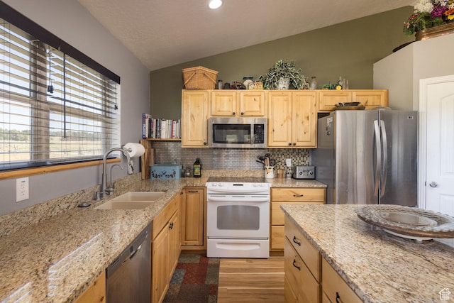 kitchen featuring light brown cabinets, appliances with stainless steel finishes, lofted ceiling, and a sink