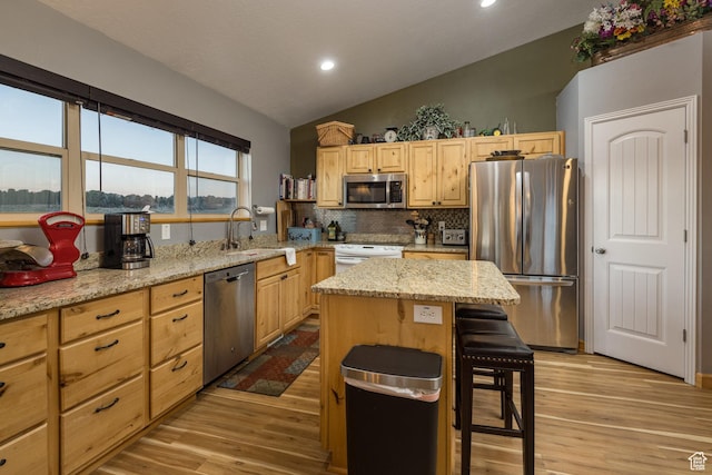 kitchen with vaulted ceiling, light brown cabinets, appliances with stainless steel finishes, and a sink