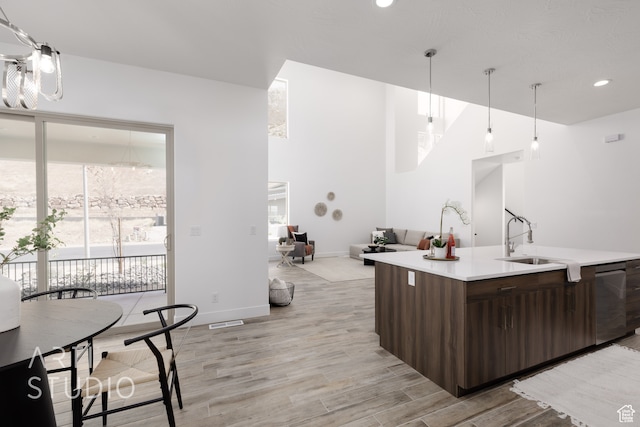 kitchen with sink, hanging light fixtures, stainless steel dishwasher, dark brown cabinetry, and light wood-type flooring
