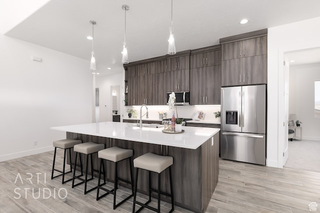 kitchen featuring sink, decorative light fixtures, a center island with sink, stainless steel appliances, and light hardwood / wood-style floors