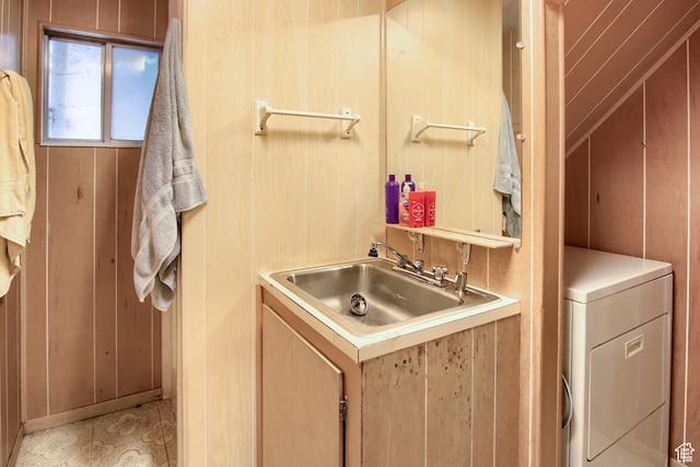 clothes washing area with wooden walls, washer / dryer, light tile patterned floors, and sink