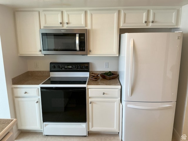 kitchen featuring freestanding refrigerator, electric stove, stainless steel microwave, and white cabinetry