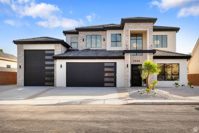 prairie-style house featuring stone siding, stucco siding, an attached garage, and concrete driveway
