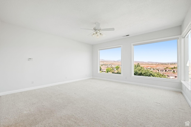 unfurnished room with carpet floors, visible vents, a ceiling fan, a textured ceiling, and baseboards