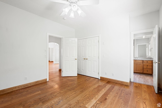 unfurnished bedroom with light wood-type flooring, baseboards, arched walkways, and a closet