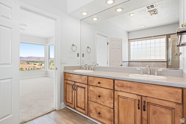 full bath with double vanity, a textured ceiling, visible vents, and a sink