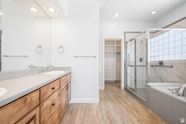 full bath featuring wood finished floors, a sink, a spacious closet, a marble finish shower, and double vanity