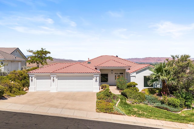 mediterranean / spanish-style house featuring a garage, concrete driveway, a tiled roof, a mountain view, and stucco siding