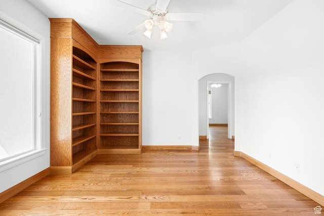 spare room with arched walkways, ceiling fan, light wood-type flooring, and baseboards