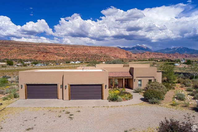pueblo revival-style home with stucco siding, a mountain view, gravel driveway, and a garage