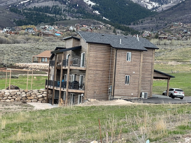 view of side of home featuring central AC unit, a mountain view, roof with shingles, and a balcony