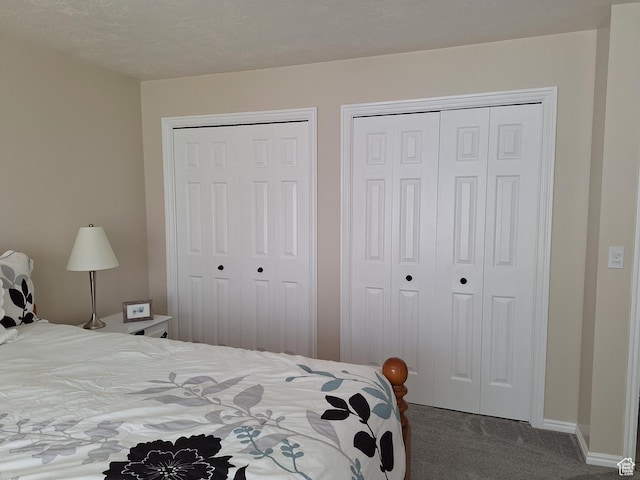 bedroom with a textured ceiling, two closets, baseboards, and carpet floors