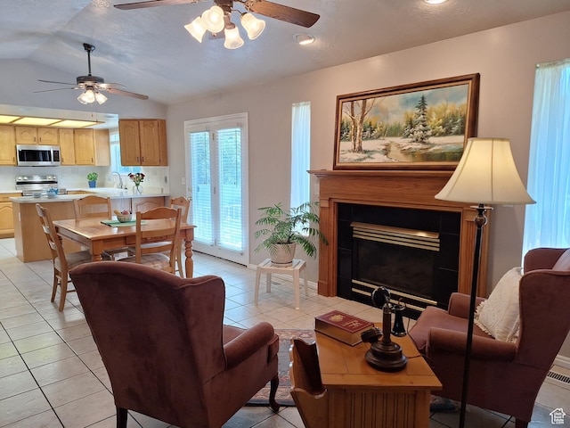 living area featuring light tile patterned flooring, baseboards, ceiling fan, vaulted ceiling, and a tile fireplace