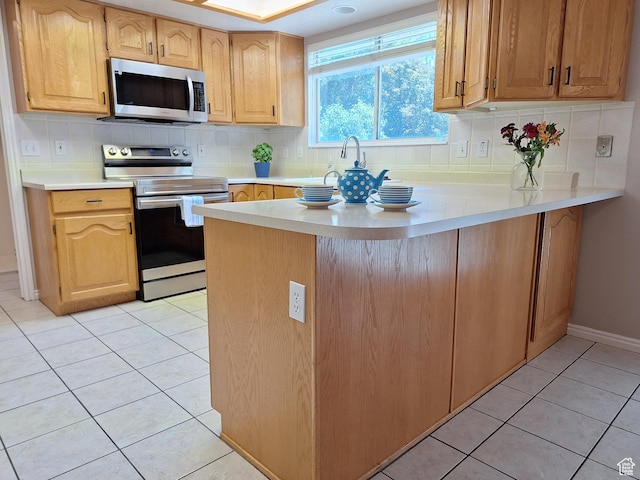kitchen with light countertops, light tile patterned flooring, a peninsula, and appliances with stainless steel finishes