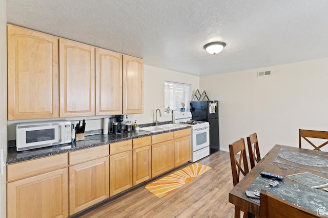 kitchen featuring visible vents, a sink, white appliances, light brown cabinetry, and light wood-style flooring