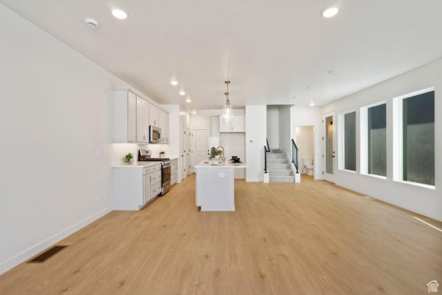 10033 N Torreya Dr Unit 737, Highland, UT 84003 - kitchen featuring appliances with stainless steel finishes, an island with sink, open floor plan, light wood finished floors, and recessed lighting